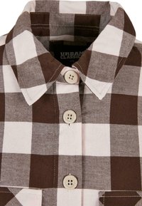 Camisa a cuadros marrón y blanca con cuello abotonado, dos botones en la parte delantera y una tela texturizada. Etiqueta: Urban Classic, talla XS.