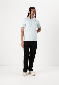 Hellblaues Baumwoll-T-Shirt mit kurzen Ärmeln, kombiniert mit schwarzen Hosen und beigen Sneakers. Einfaches Design, keine sichtbaren Muster oder Logos.