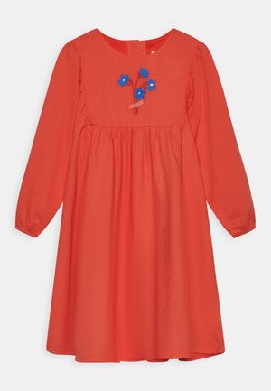 Robe rouge à manches longues en tissu texturé, ornée de broderies florales bleues sur le corsage, avec un col rond et une fermeture à boutons dans le dos.