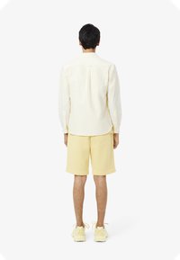 Camicia gialla chiara a righe con bottoni abbinata a pantaloni corti gialli solidi, indossata con sneakers gialle coordinate, vista da dietro.