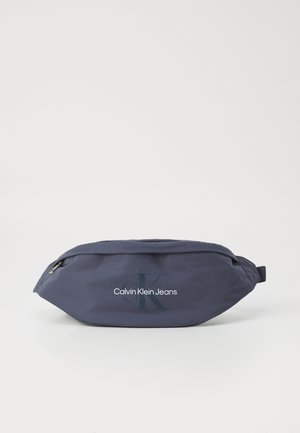Marineblå stoffhofteveske med glidelås, med et stort preget logo "Calvin Klein Jeans" og et stilisert "CK" i mørkegrønn.