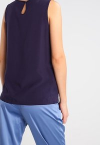 Mörknavy ärmlös topp med en nyckelhålsdetalj i ryggen, tillverkad av mjukt tyg. Matchad med ljusblå satinsbyxor.