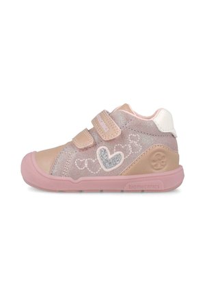 Pequeño zapato rosa para niño pequeño con dos tiras de velcro, bordado de corazón y suela de goma sobre fondo blanco.