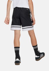 Zwarte sportshorts met witte bies en twee horizontale strepen, elastische tailleband en soepel materiaal. Gedragen met zwart-witte gestreepte sokken.