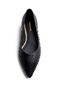 Scarpa piatta in pelle nera con punta appuntita, caratterizzata da piccoli borchie nere sulla superficie. Interno foderato con logo dorato visibile.