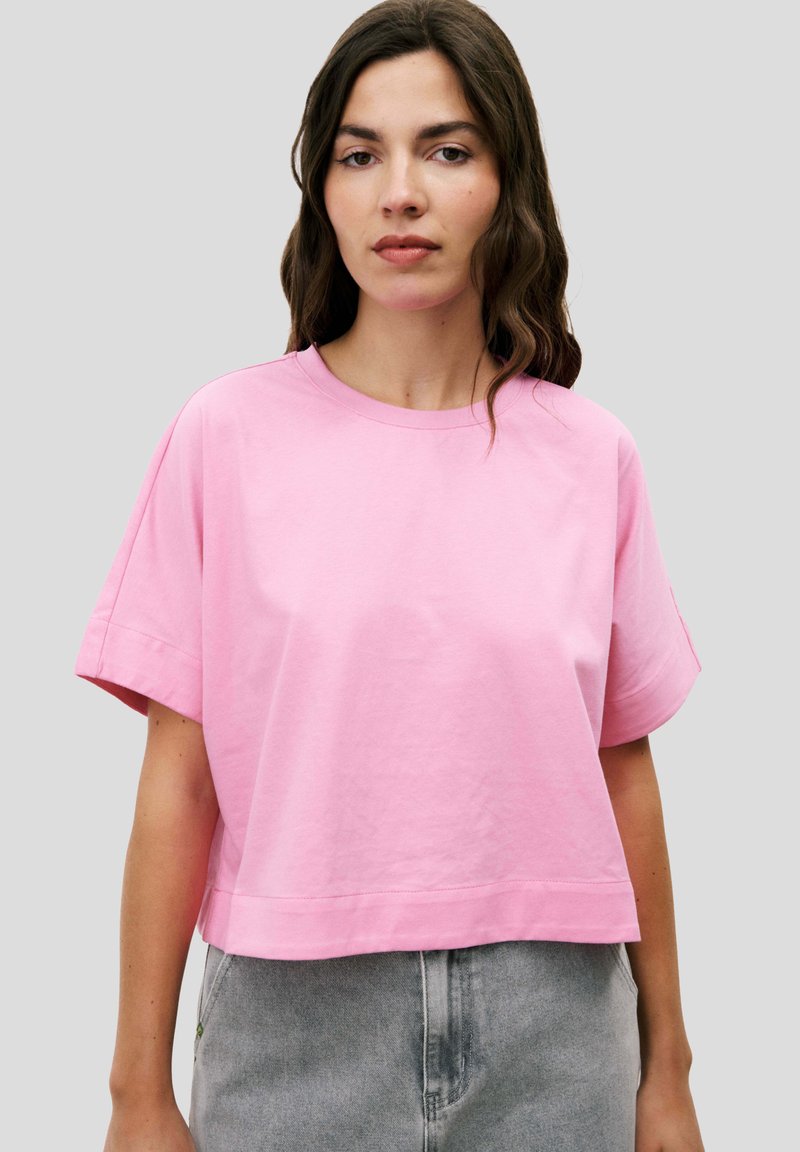T-shirt cropped rose en coton, avec un col rond et des manches courtes, offrant une coupe décontractée. Texture lisse, design minimaliste.