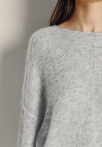 Soft gray knit sweater worn by a person, showing upper torso and neck with long brown hair against plain background.