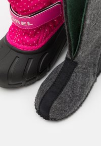 Bota impermeable de lunares rosas con suela de goma negra, combinada con una bota de fieltro gris tipo slip-on con una franja de tela negra a lo largo del costado.