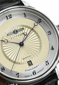 Zeppelin watch with a textured cream dial, silver-tone case, blue hands, date display at 6, and brown leather strap. Marked "Friedrichshafen."