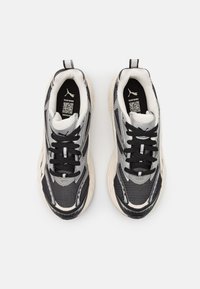 Une paire de baskets Puma noires, grises et blanches avec des lacets noirs, une tige en mesh et synthétique, et des tirettes sur fond blanc.