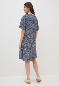 Vestito navy con motivo a foglie bianche, maniche corte e taglio rilassato. Stile casual, indossato con sneakers di colore chiaro.