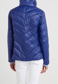 Blå puffjacka med hög krage och Chevron-quiltmönster. Glansig yta, strukturerad passform och elastiska ärmslut.