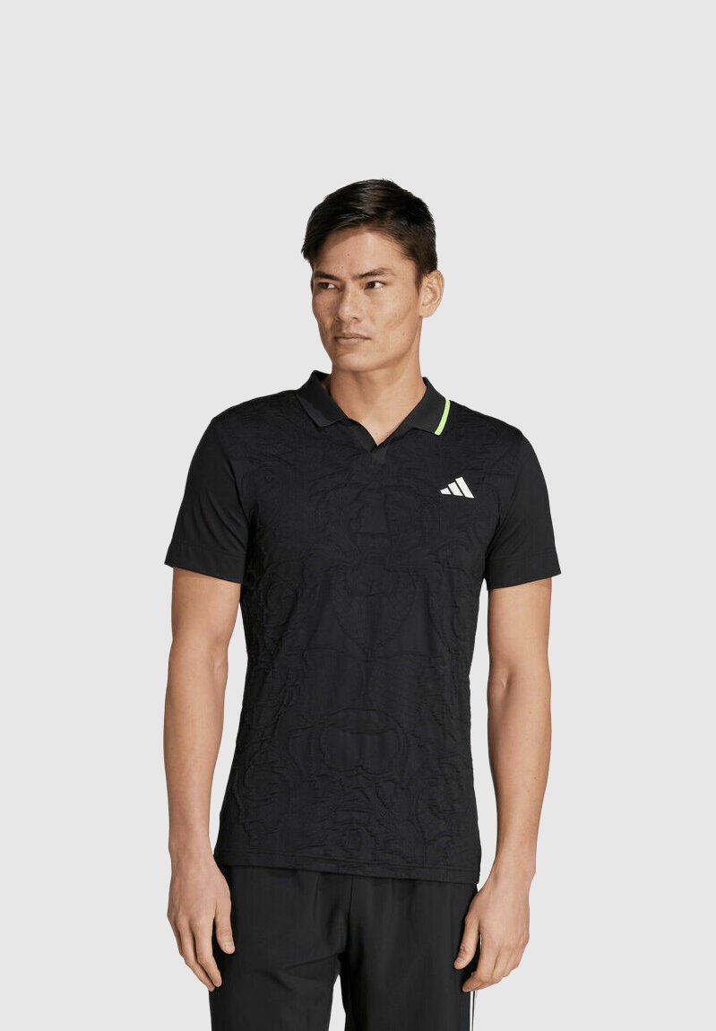 Polo negro de manga corta con un patrón texturizado, un cuello negro con un acento verde y un logo de Adidas en el lado izquierdo del pecho.