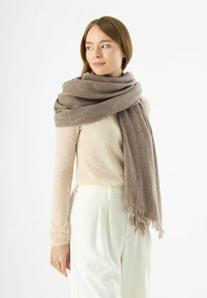 Sciarpa in misto lana con sfumature di marrone morbido, con orli sfrangiati, avvolta attorno al collo e abbinata a una maglietta beige chiaro e pantaloni bianchi.