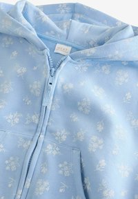 Lyseblå hættetrøje med blomsterprint i hvid, frontlynlås og kængurulomme. Fremstillet af blødt stof, med en hætte der har snore.