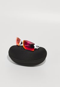 Białe okulary przeciwsłoneczne z gradientowymi różowo-pomarańczowymi soczewkami w czarnym, okrągłym twardym etui. Posiadają zaokrąglone ramiona i elegancki design.