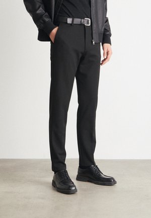 Black tailored pants with a sleek design, accompanied by a black leather belt and black lace-up shoes, set against a neutral background.