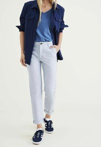 Marine knoop-overhemd boven een blauwe V-hals t-shirt, gecombineerd met licht gestreepte broek en marine sneakers. Katoenmix; relaxte pasvorm; opgerolde mouwen.