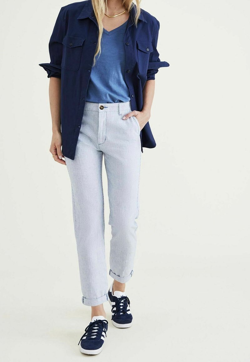 Marine knoop-overhemd boven een blauwe V-hals t-shirt, gecombineerd met licht gestreepte broek en marine sneakers. Katoenmix; relaxte pasvorm; opgerolde mouwen.