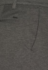 Pantalons en tissu gris avec une finition texturée, dotés d'une poche arrière et d'un petit logo noir. Design ajusté avec une silhouette épurée.