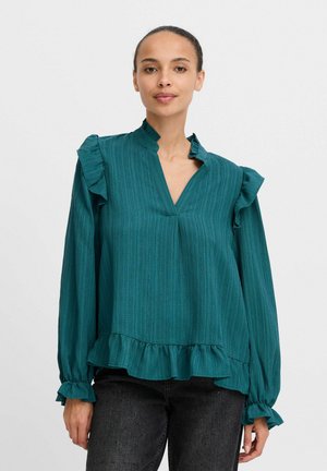 Tamsiai mėlynas ilgomis rankovėmis blusas su volaniniu apykakle ir rankogaliais. Vertikalūs dryžių raštai ir platėjanti apačia suteikia subtilių detalių.