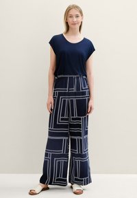 Navy blue t-shirt with a round neckline paired with wide-leg pants featuring a geometric white pattern and elastic waistband. White sandals.
