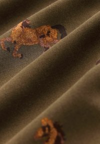 Brunt stof med et lille, detaljeret mønster af orange og mørkebrune løver, vist i bløde folder.