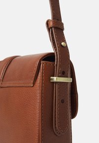 Bolsa de mão em couro castanho com um acabamento texturizado, forma estruturada e alça destacável com ferragens em latão e um bordado intricado.