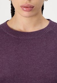 Violetinė megzta palaidinė su apvaliu kaklu ir smulkiais rankogaliais. Audinys yra minkštas ir šiek tiek pūkuotas, su švelniu marmurinio rašo akcentu.