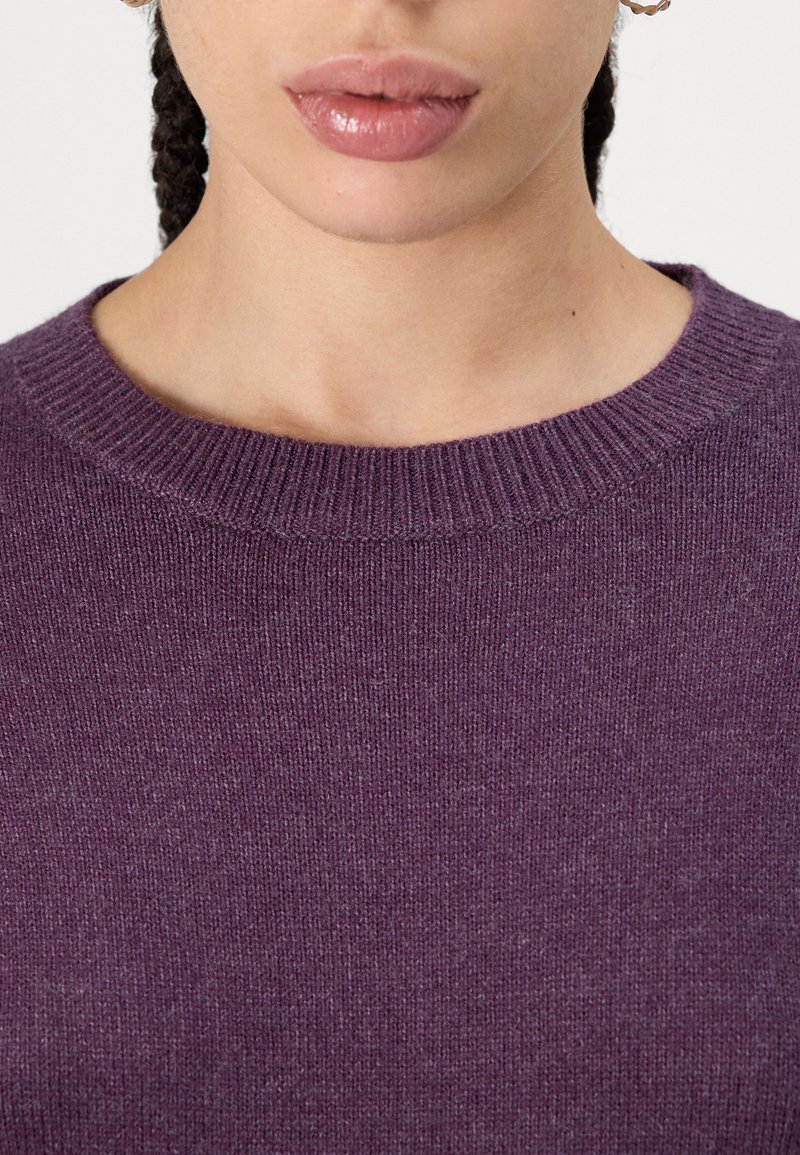 Lila gestrickter Pullover mit rundem Halsausschnitt und gerippten Bündchen. Die Textur ist weich und leicht fusselig, mit einem dezenten Melange-Muster.