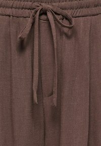 Pantalon en tissu de lin brun avec une ceinture élastique et un cordon noué au centre devant.