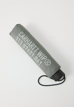 Ombrello compatto in tessuto verde scuro, con testo bianco "CARHARTT WIP" e numeri. Include un manico nero e un cordino per il trasporto.