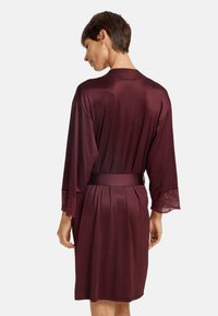 Burgundy silkrok med spetsdetaljer på ärmarna, bälte i midjan och knälång längd. Slät textur med en avslappnad passform.