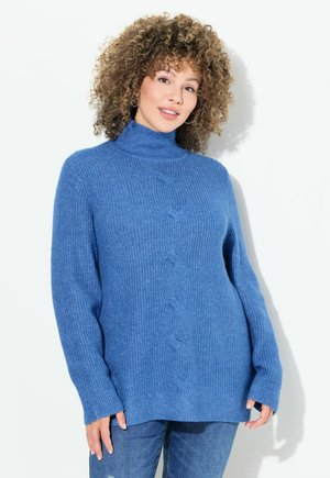 Světle modrý, silný pletený svetr s vysokým límcem, volným střihem a cable knit vzorem vpředu, spárovaný s džínovými kalhotami.