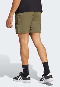Khaki cargo shorts with side pockets and a straight cut, worn with black socks and black sneakers with white stripes. Short length.