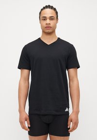 Μαύρο κοντομάνικο T-shirt με V-λαιμό που είναι φτιαγμένο από μαλακό βαμβάκι, διαθέτοντας μια διακριτική λευκή λογότυπο της Adidas στο κάτω αριστερό μέρος.