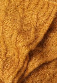 Coperta lavorata a maglia in morbida lana gialla senape con una trama a treccia, caratterizzata da una superficie leggermente pelosa per un calore aggiuntivo.