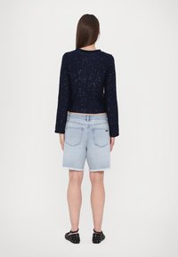 Marineblå cropped genser med strukturert strikk og sølvflekker, kombinert med lyseblå denimshorts med frayed kant og baklommer.