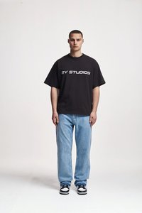 Black oversized t-shirt with "2Y STUDIOS" printed in white, paired with light blue relaxed-fit jeans and black and white sneakers.