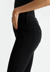 Jeans in denim nero con un design aderente, dotati di vita media, tasche laterali e dettagli di cucitura sottili. Tessuto liscio.