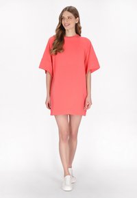 Korall színű, oversized pólóruha rövid ujjakkal, puha anyagból készült. Kerek nyakkivágású és laza szabású, a térd felett ér véget.