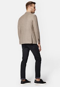 Jasnobrązowa, fakturowana marynarka z klapami, w zestawieniu z czarnymi, dopasowanymi dżinsami oraz czarnymi, fakturowanymi sneakerami. Widoczne detale mankietów na marynarce.