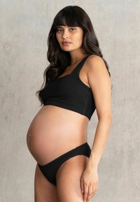 Conjunto de sujetador premamá negro acanalado y braguita bikini a juego, con un diseño ajustado, tirantes anchos y textura de tela suave, que resalta una silueta de embarazada.