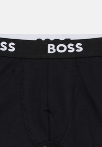 Μαύρα αντρικά εσώρουχα τύπου μπόξερ με μαύρη ελαστική μέση που φέρει το λευκό κείμενο της μάρκας "BOSS" στο κέντρο εμπρός.