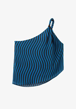 Žena v modro-čiernom jednoramennom vlnovkovom prúžkovanom topu, svetlomodrých džínsach s širokými nohavicami a čiernych sandáloch, stojaca na jednoduchom pozadí.