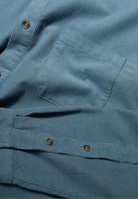 Knopenoverhemd van gestructureerde blauwe stof. Kenmerkt een borstzak, bruine knopen en een rechte zoom met een eenvoudig ontwerp.