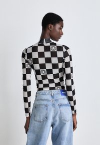 Long-sleeve top in black and white checkerboard pattern with graphic accents. Paired with light blue denim jeans featuring a logo waistband.
