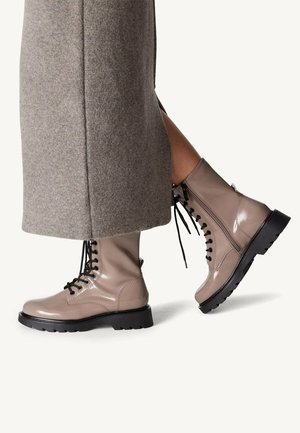 Bottes de cheville en cuir verni beige clair avec des lacets noirs, semelles en caoutchouc épaisses et zips latéraux, associées à une jupe en laine grise.