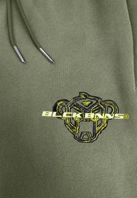 Groene hoodie met een zwart en gele geborduurde dierenmaskerlogo en tekst, met zilveren trekkoorden. Zachte, gestructureerde stof.