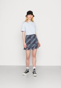 Camiseta azul claro, saia larga azul-marinho com bainha em babados e chapéu preto tipo balde. Ténis de cano alto preto e branco com atacadores.